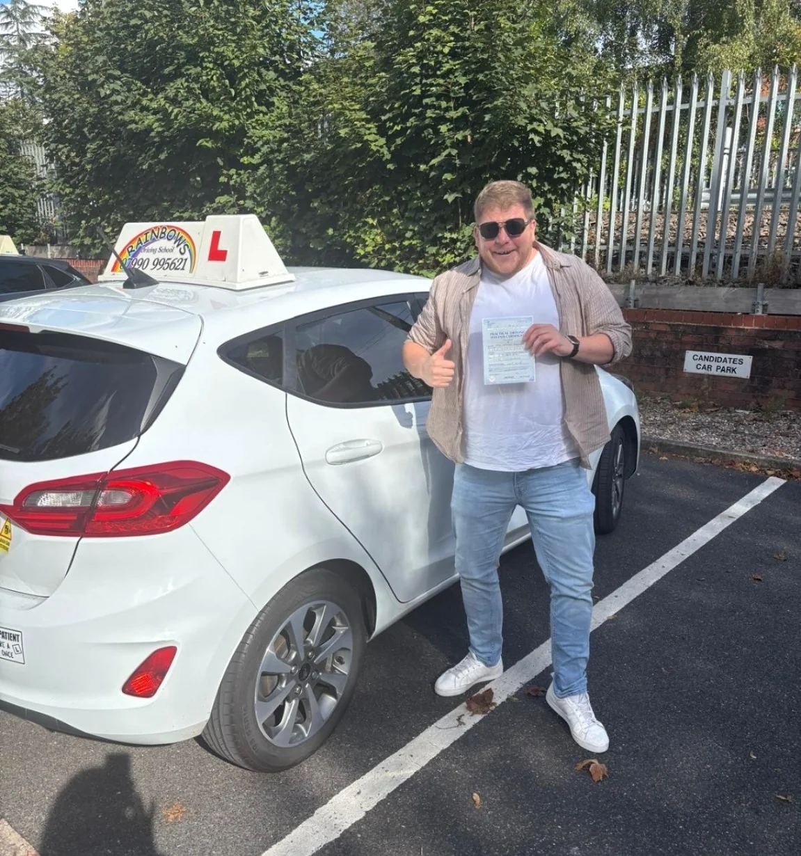 Craig celebrating his driving test pass beside the Rainbows learner car, holding his pass certificate